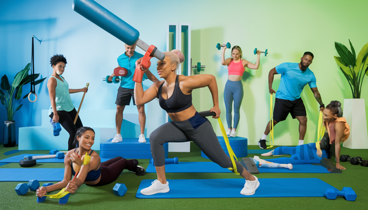 A diverse group of individuals exercising in a vibrant home gym using various fitness equipment like mats, resistance bands, dumbbells, and a massage stick.